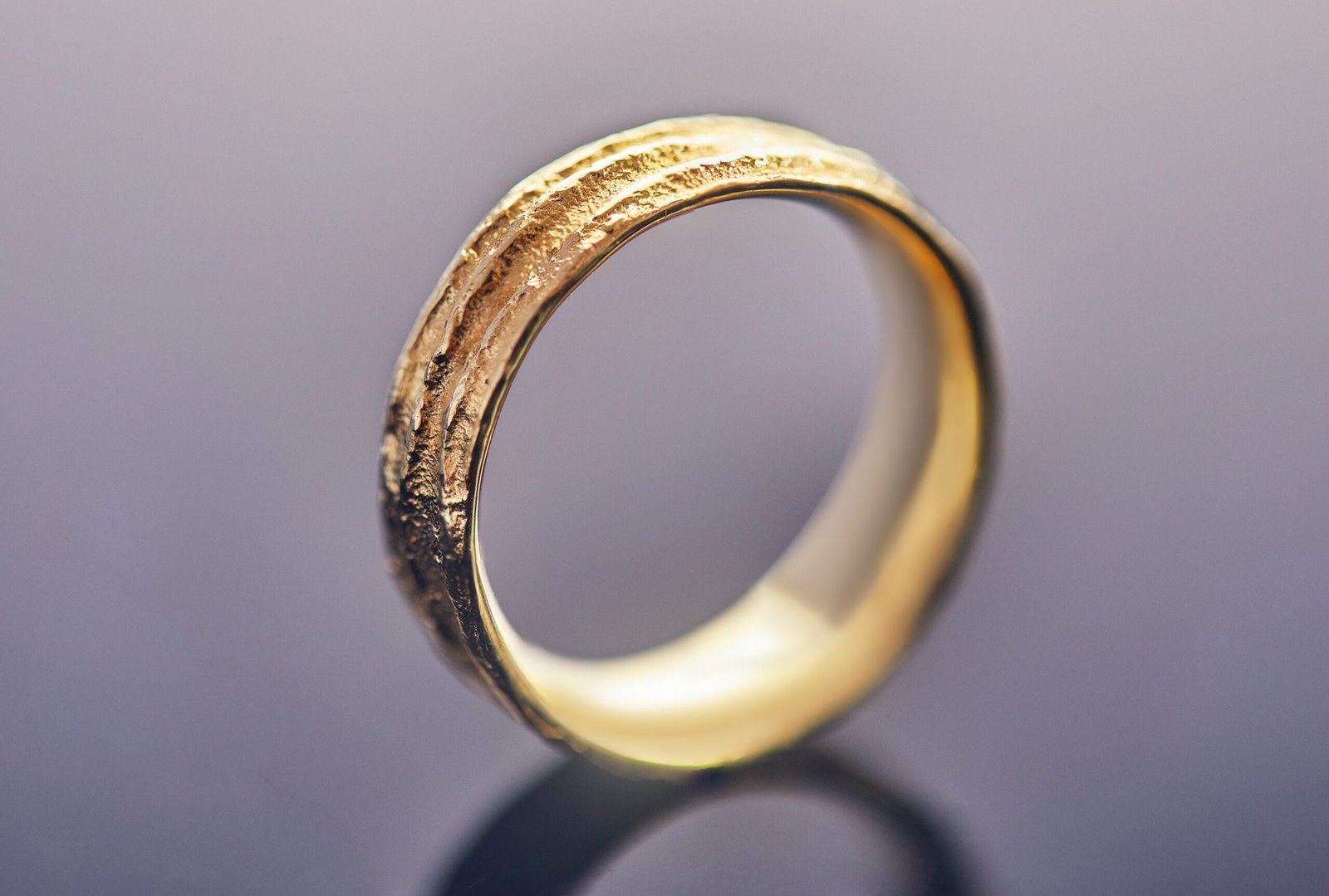 Jewelry making. Yellow gold wedding ring with an unusual texture standing on a gray background.